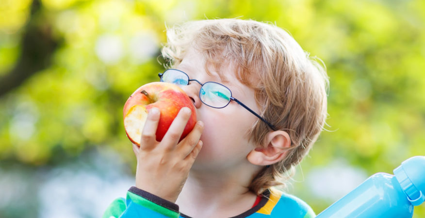 Bambino con occhiali che mangia una mela